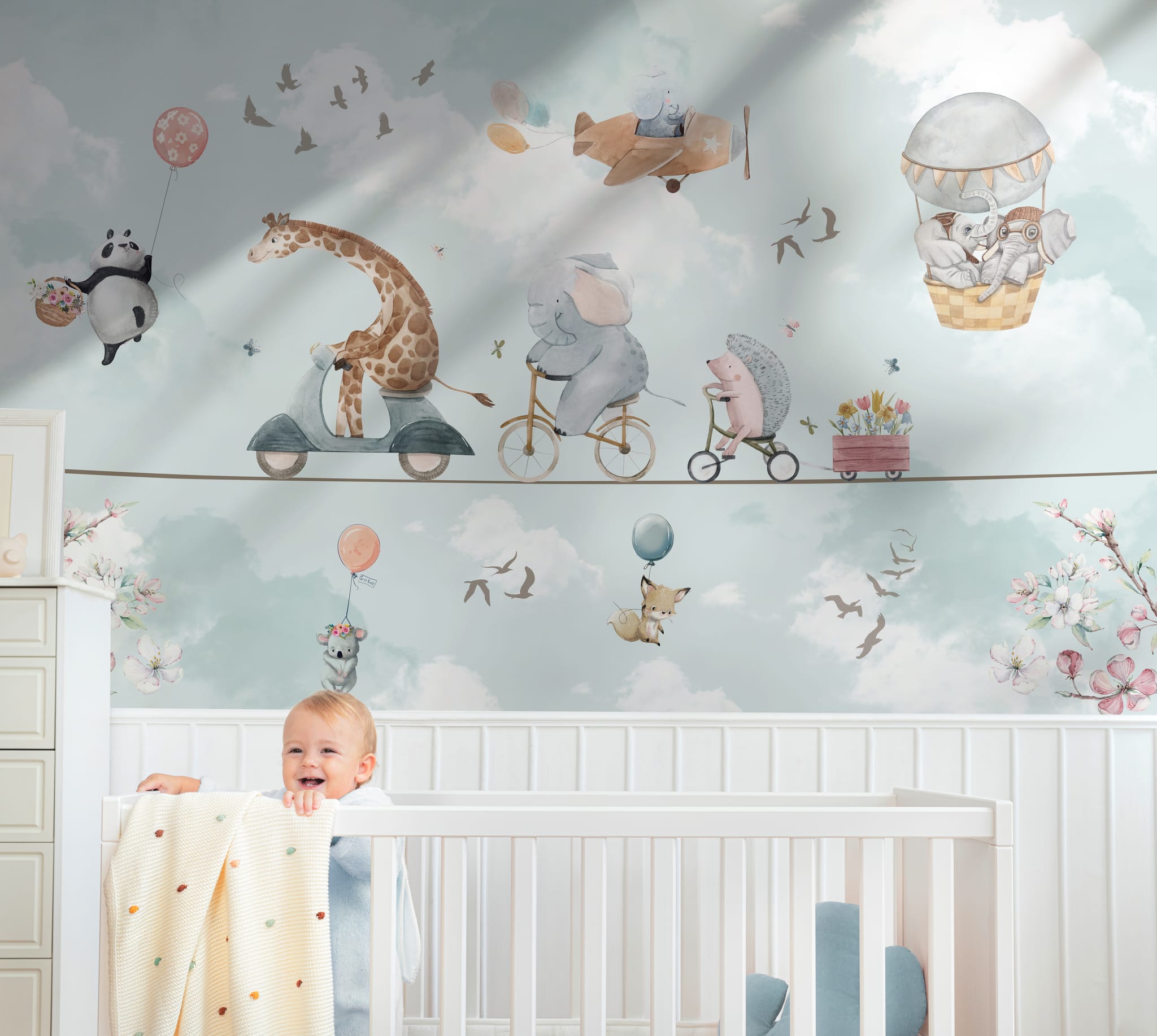 Blue watercolor animal nursery wallpaper with giraffe, elephant, panda, hedgehog, clouds, and balloons behind a white crib